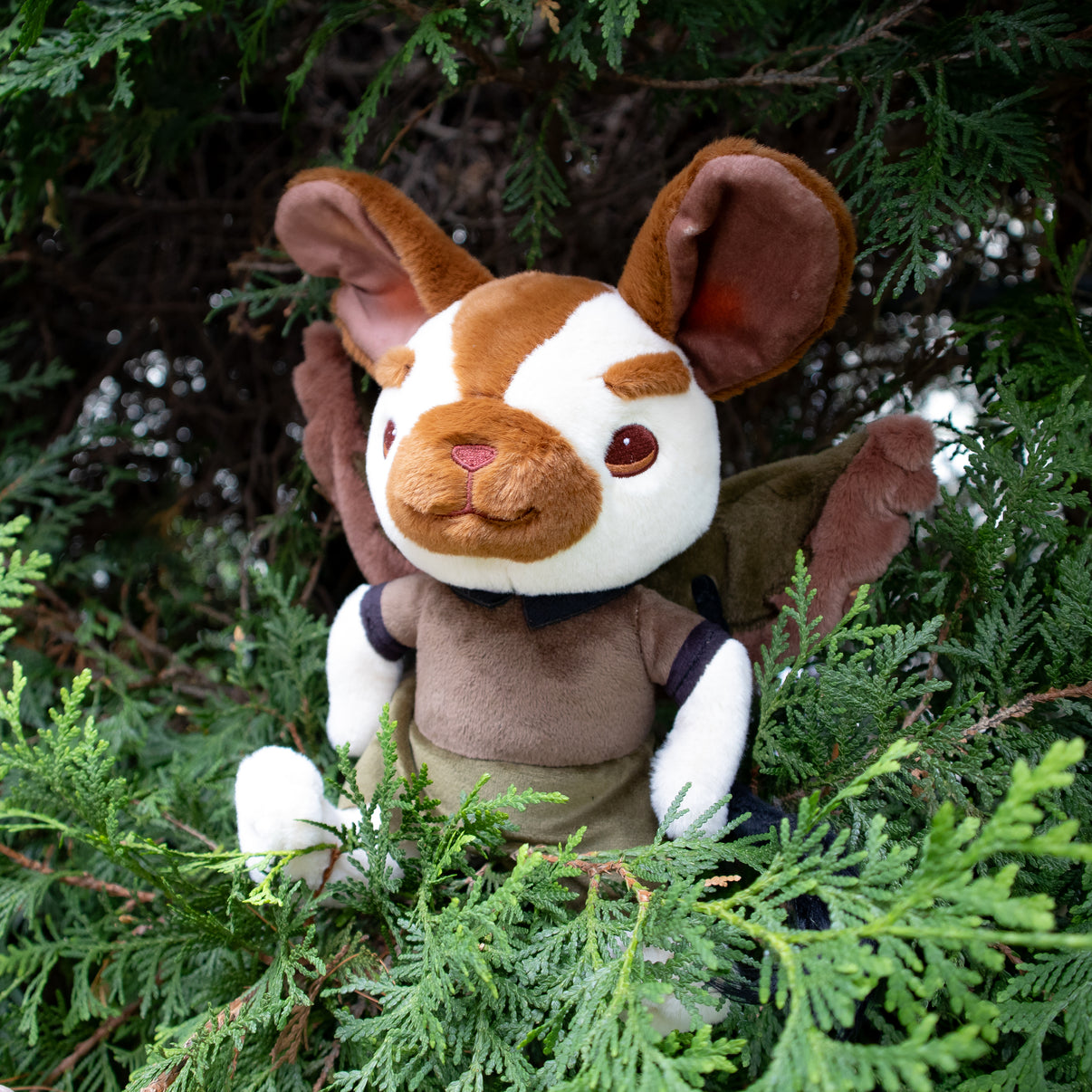 Plush toy resembling a mouse with wings sitting among green foliage