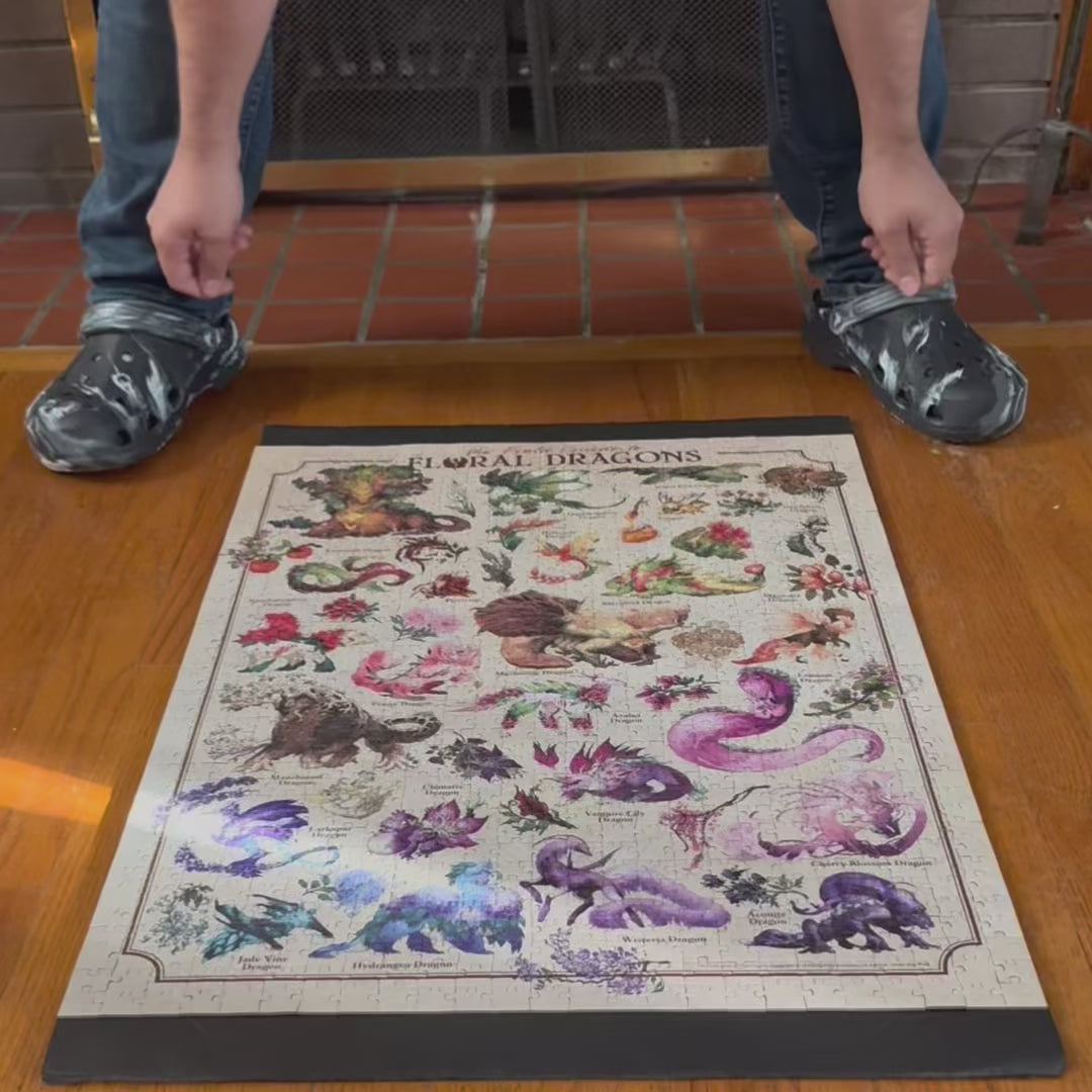 A person carefully lifts a fully completed Floral Dragons puzzle, to show to the viewer.